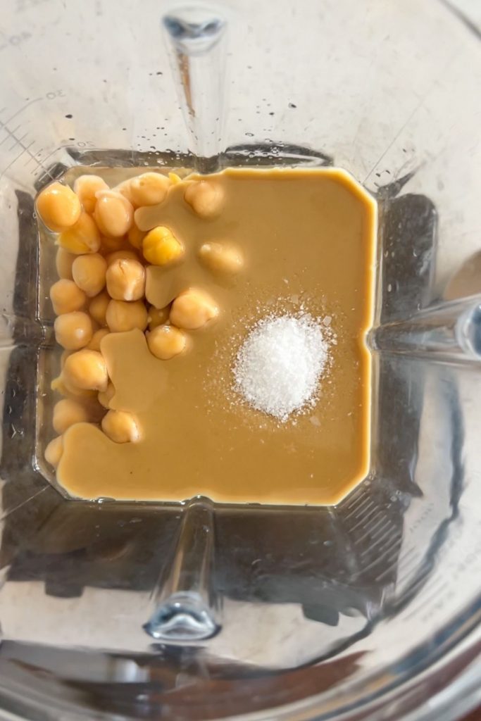 The view inside a blender with chickpeas, tahini, lemon juice, salt and water.