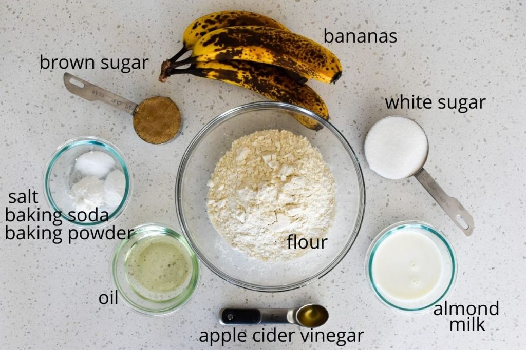Picture of the the ingredients for banana muffins without eggs: bananas, white sugar, brown sugar, almond milk, apple cider vinegar, oil, flour, salt, baking soda and baking powder.