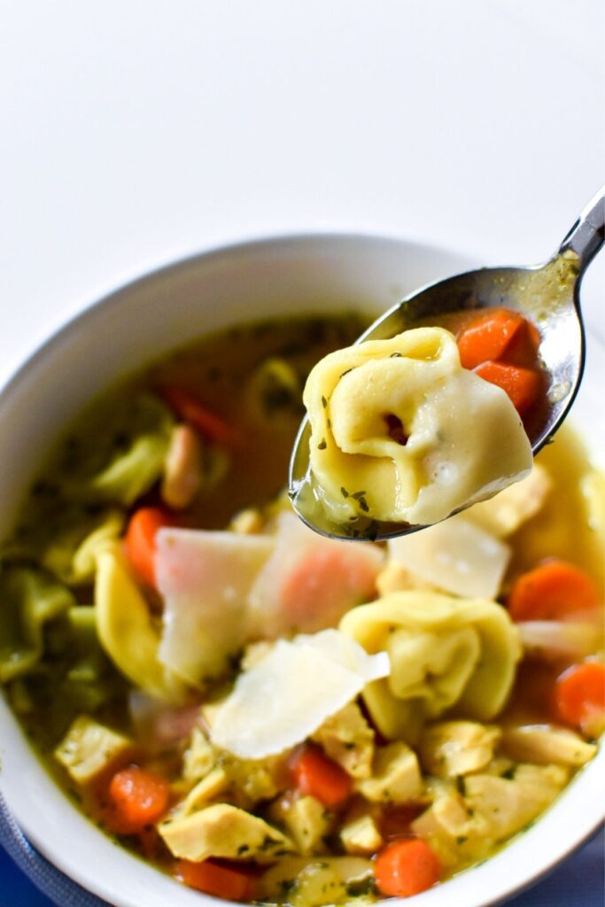 A spoon lifting tortellini and carrots out of a bowl of chicken tortellini soup.