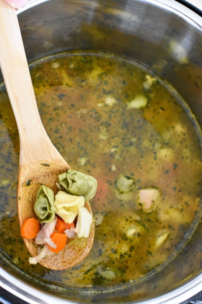 View inside an Instant Pot with a wooden spoon holding tortellini, carrots, chicken and celery.