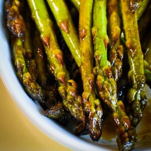 Cooked asparagus with balsamic vinegar on it in a white dish.