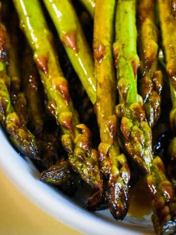 Cooked asparagus with balsamic vinegar on it in a white dish.