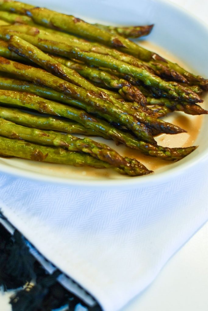 Sautéed asparagus in a balsamic vinegar reduction on a white plate with a white kitchen towel underneath.