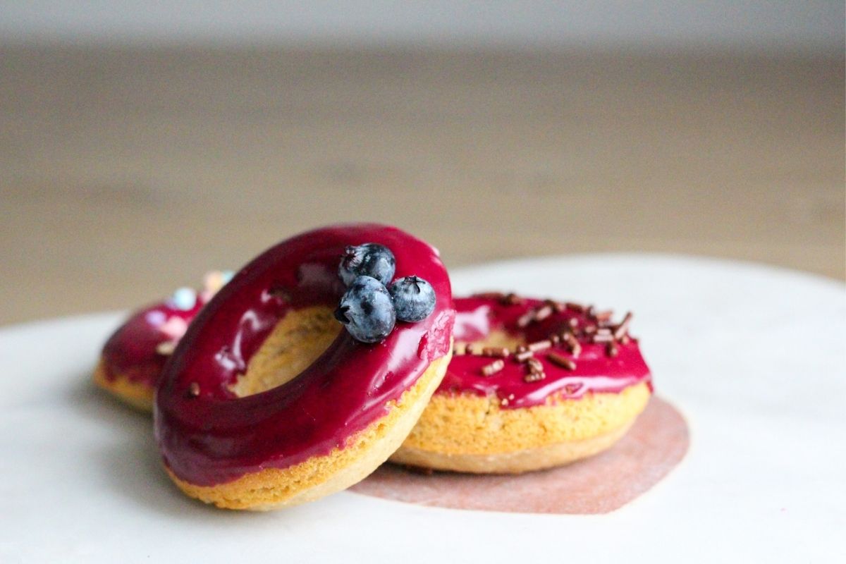 Three donuts with a homemade blueberry glaze with blueberries on top.