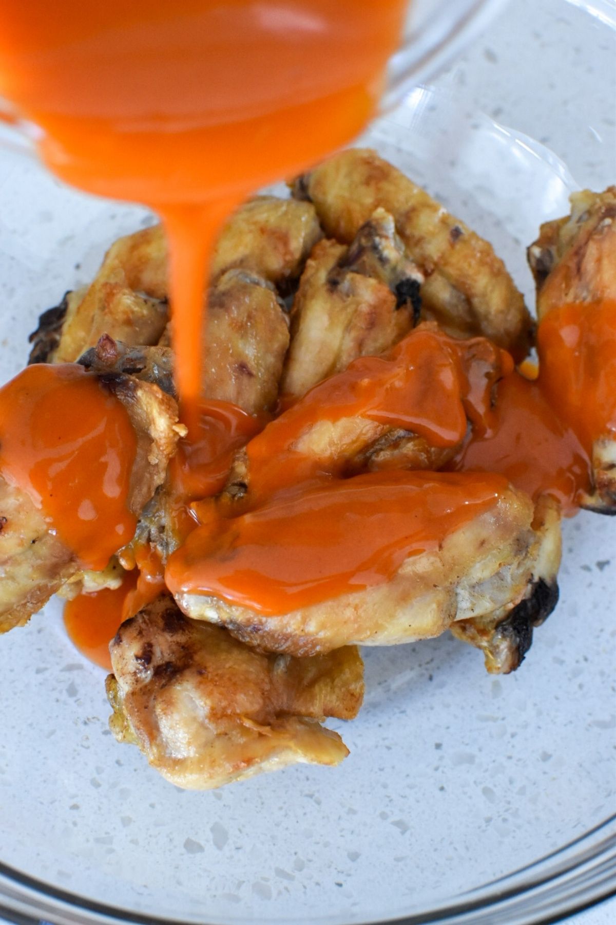 Cooked air fryer chicken wings with mild buffalo sauce being poured on top.