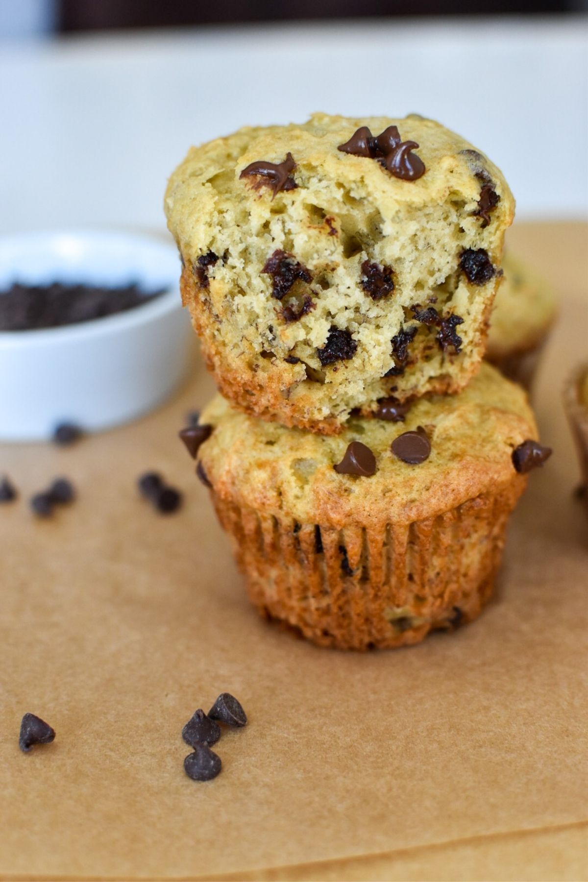 Two muffins stacked on top of each other with chocolate chips scattered around.