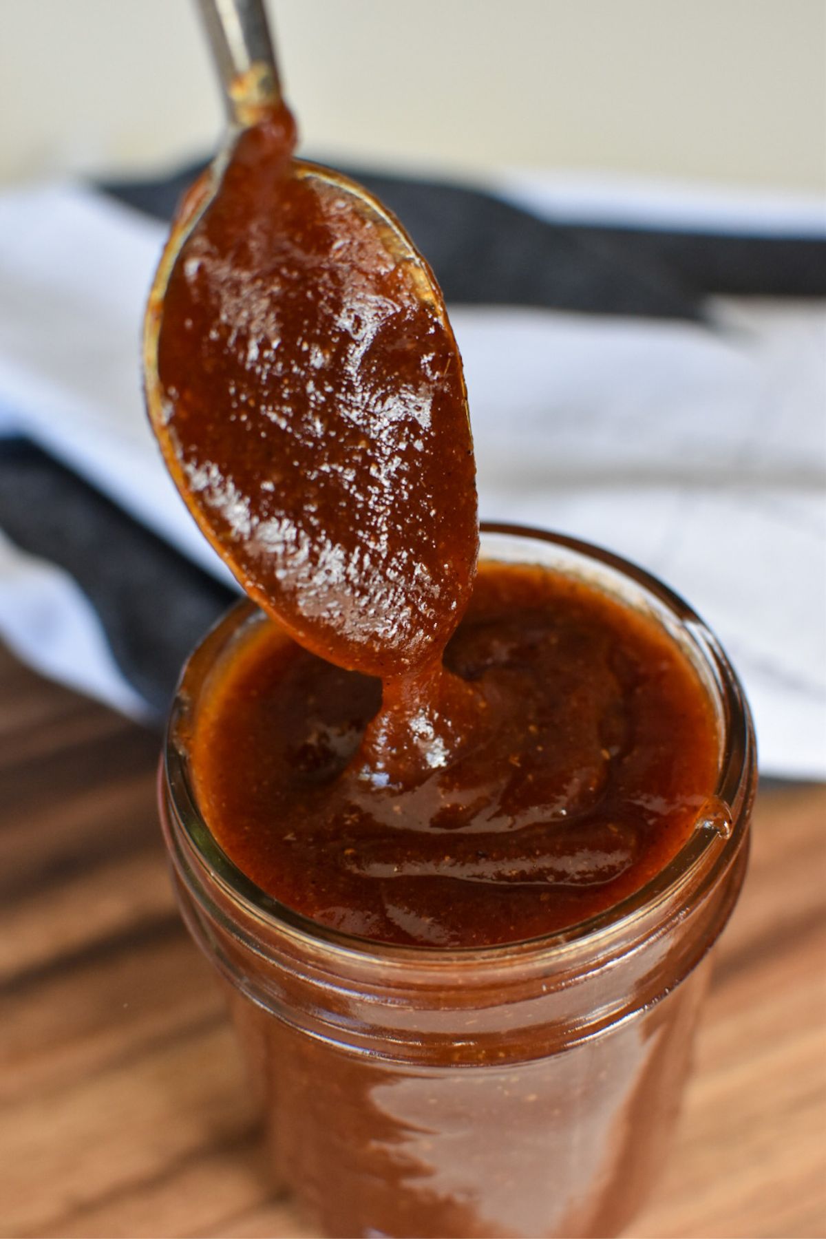 Thick-barbecue sauce falling off a spoon into a glass jar.