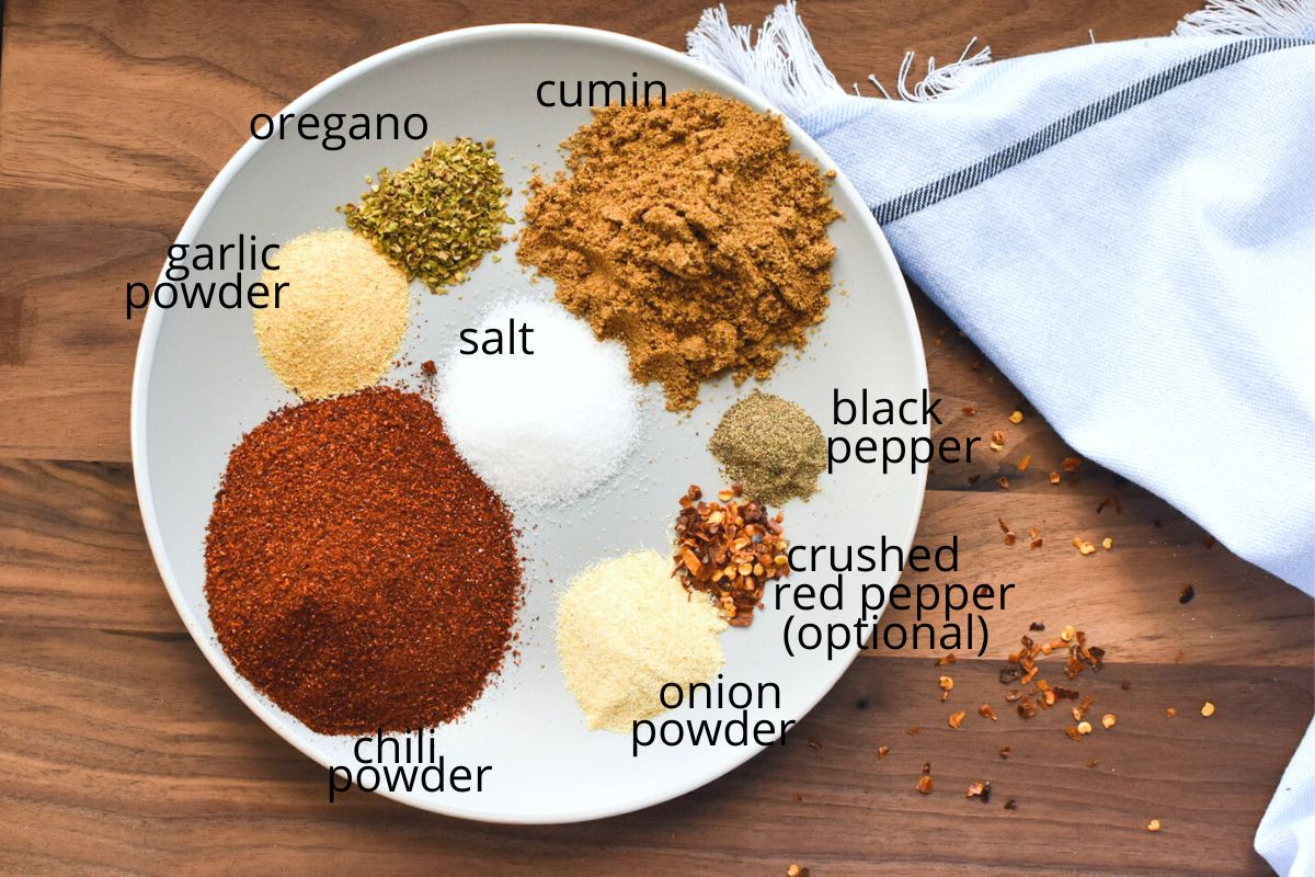 The ingredients for mild taco seasoning on a plate with a wooden cutting board below it.