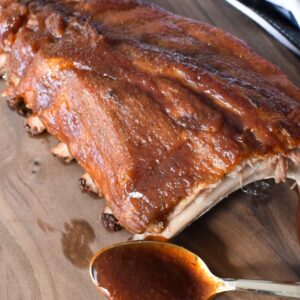 Rack of pork loin back ribs on a wooden cutting board with a spoon of bbq sauce next to them.