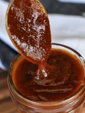 Thick-barbecue sauce falling off a spoon into a glass jar.