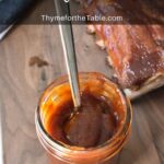 Barbecue sauce and spoon in a jar with ribs in the background and text: sweet and tangy bbq sauce.
