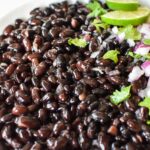 Close up picture of the cooked black beans with cilantro, red onion and lime on top.