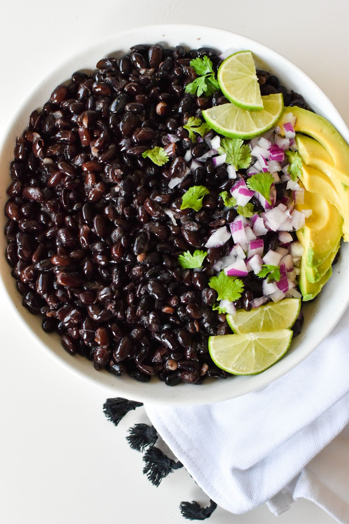 Black beans in a bowl with fresh cilantro, red onion, avocado and limes.