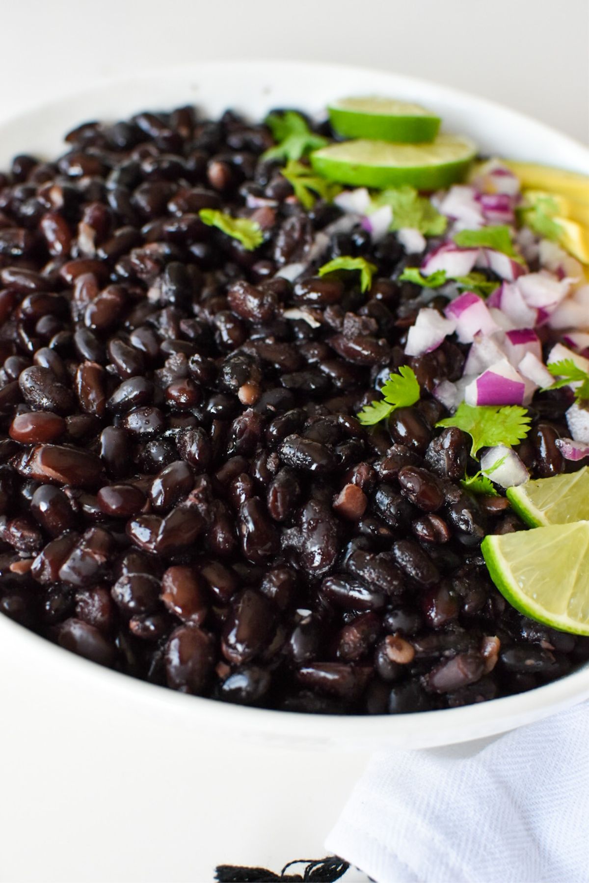 Black beans in a bowl with fresh cilantro, red onion, avocado and limes.