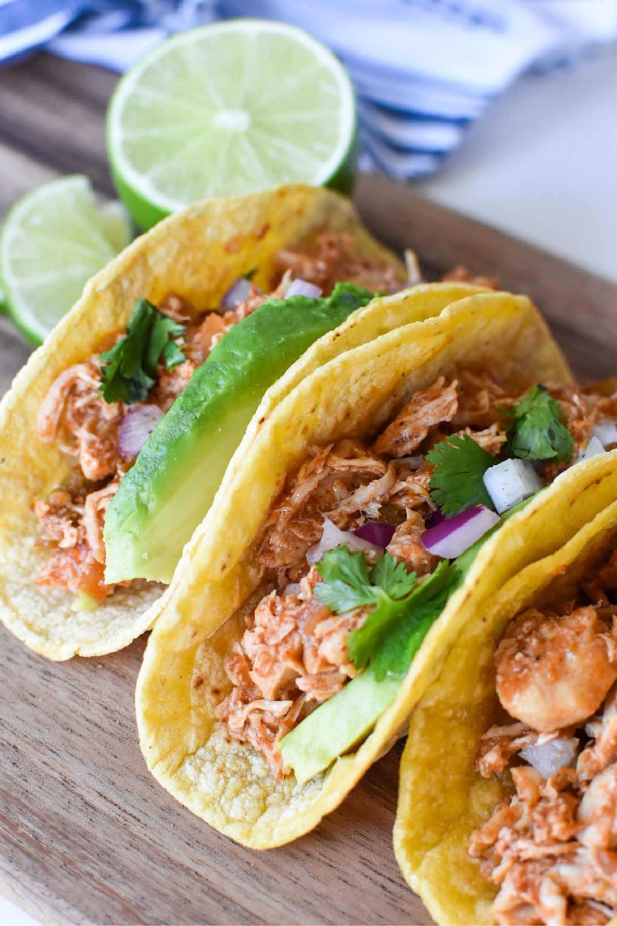 Chicken tacos on a wood board with a cut lime next to them.