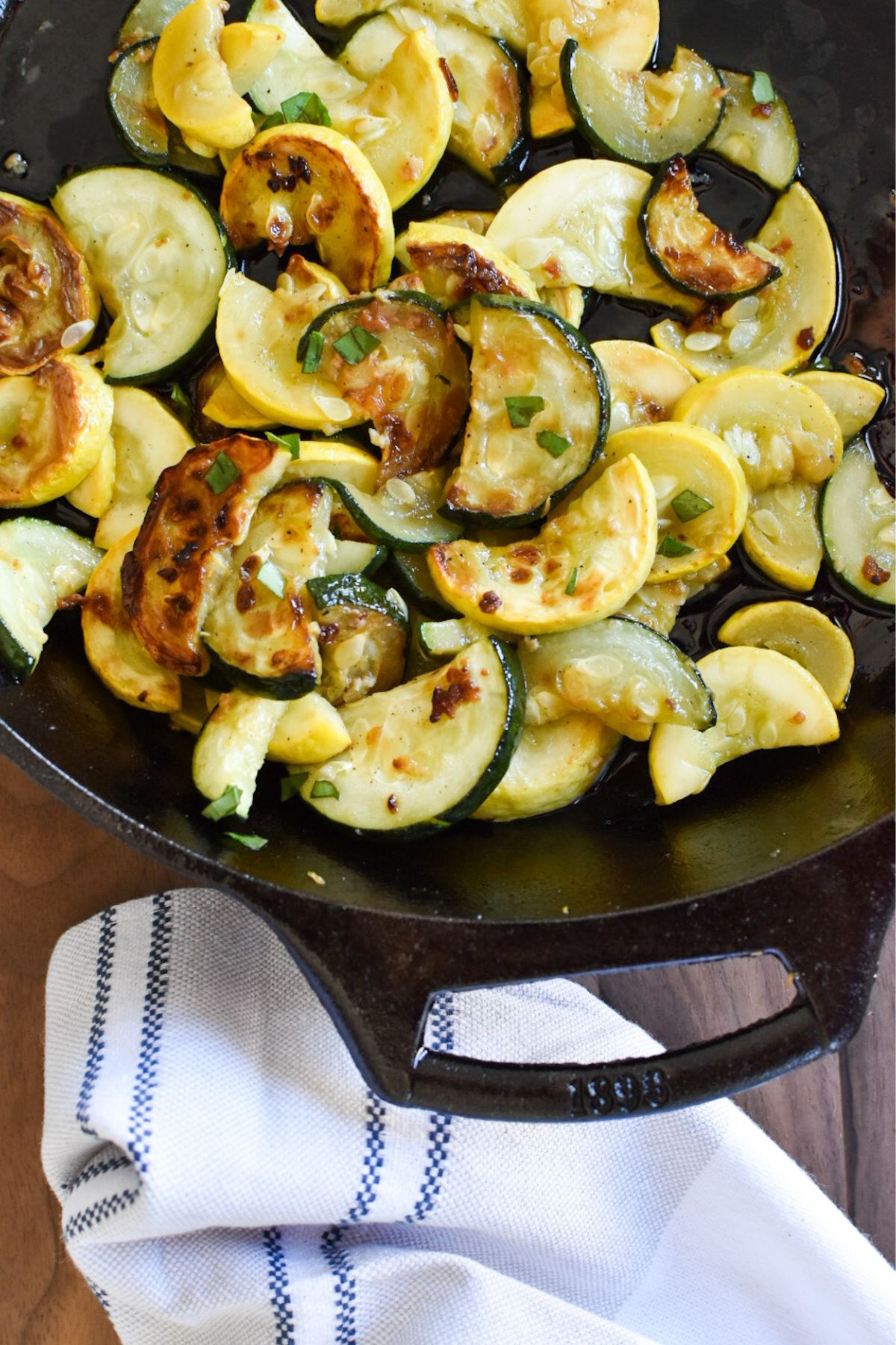Sautéed zucchini and yellow squash in a cast iron pan with towel below it.
