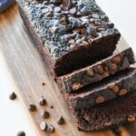 Chocolate zucchini bread on a wood board with chocolate chips next to it.