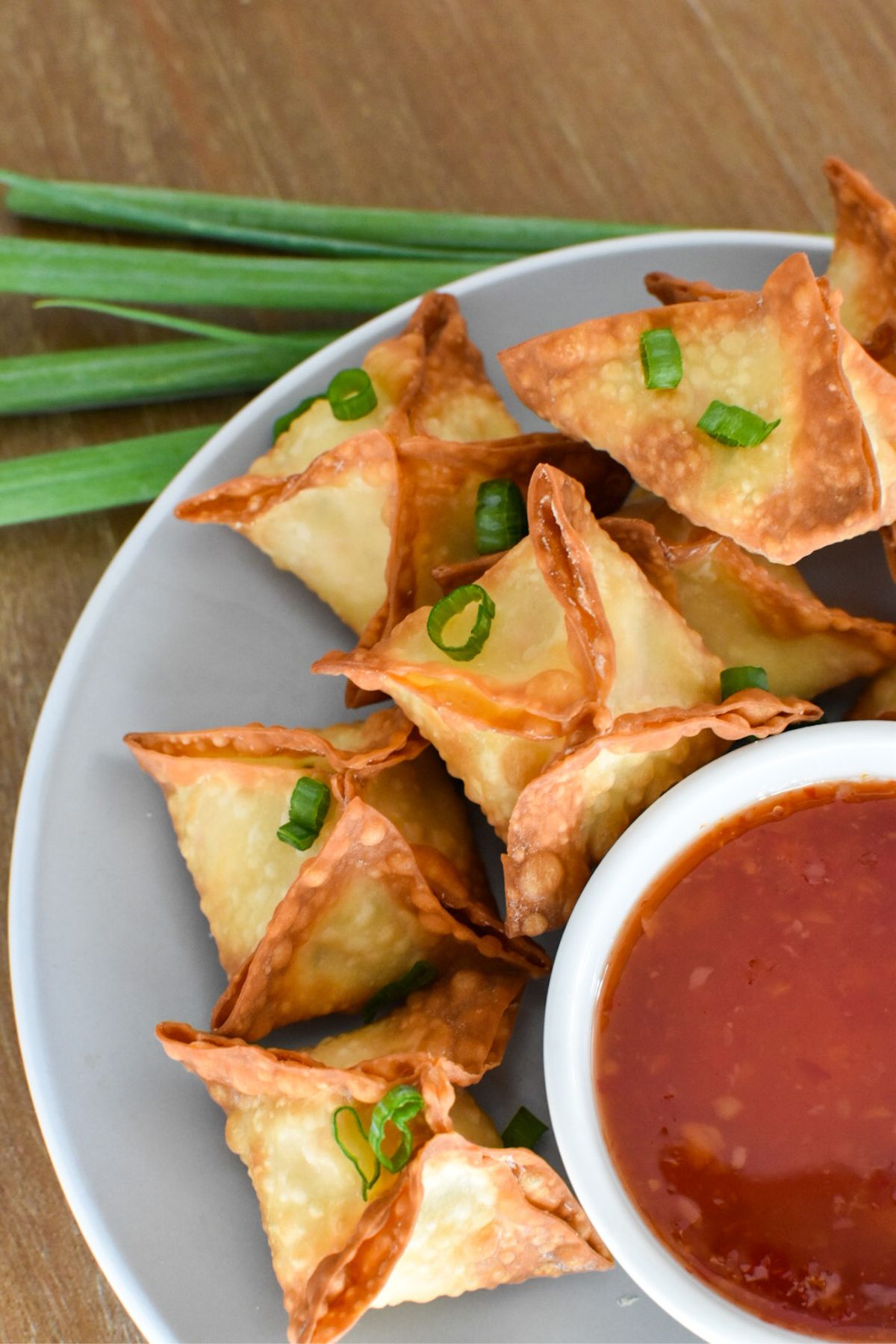 Crab rangoon stacked on a plate with a sweet chili dipping sauce next to it.