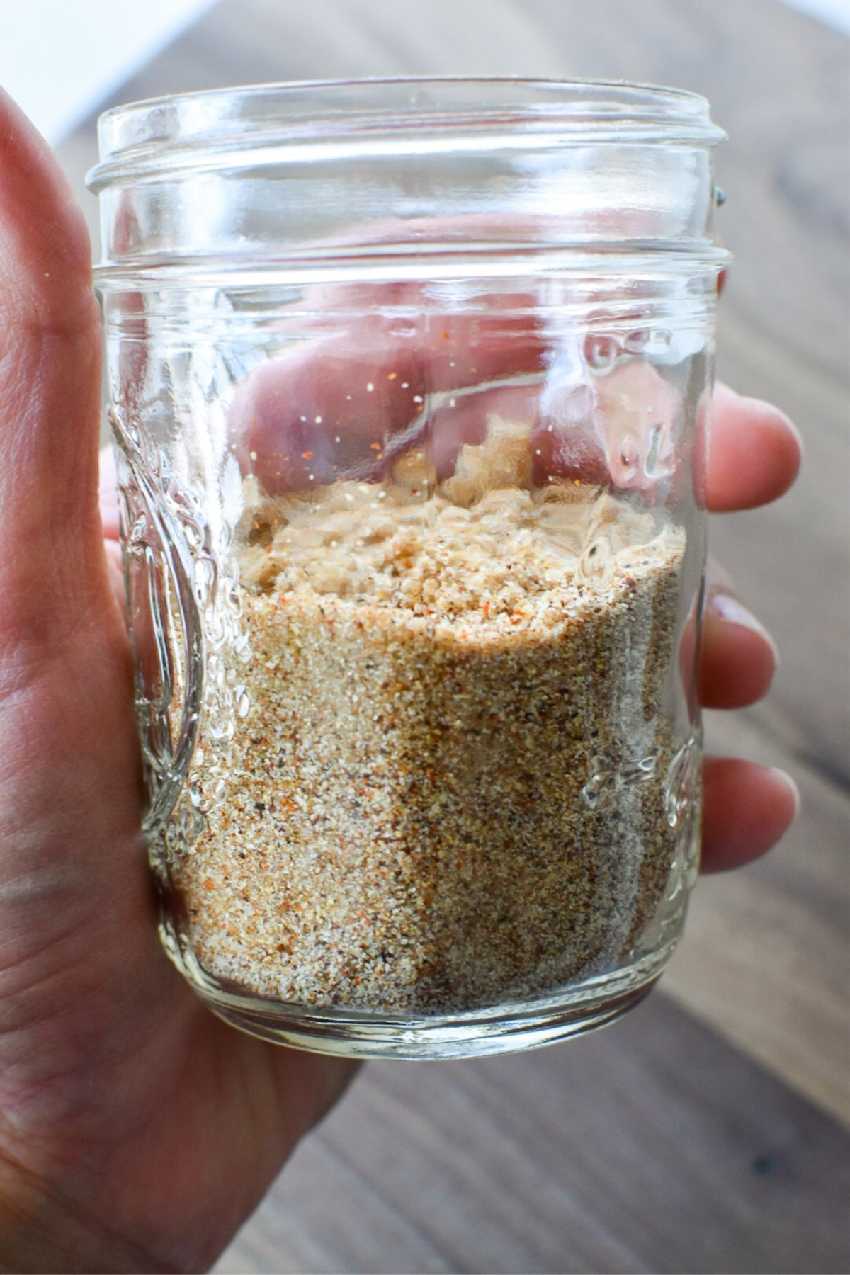 A hand holding a small glass mason jar with homemade dry rub in it.