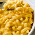 A fork scooping up creamy oven baked mac and cheese in a bowl.