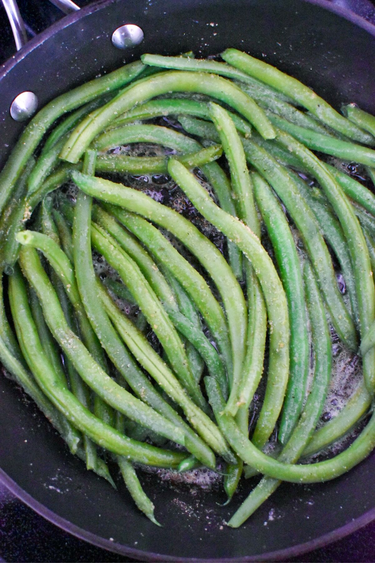 Green beans beginning to cook and soften in a sauté pan.