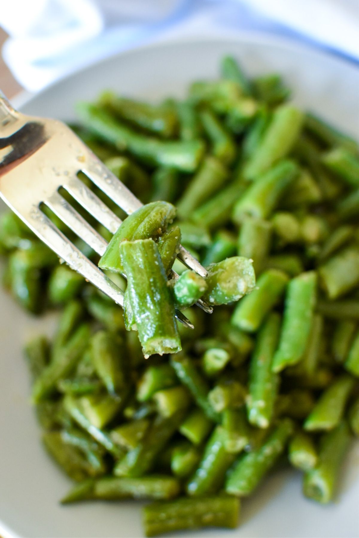 A fork holding cooked frozen green beans with a plate of green beans in the background.