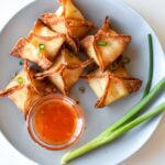 Crab rangoon on a gray plate with sweet chili sauce and green onion.