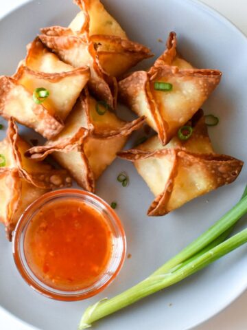 Crab rangoon on a gray plate with sweet chili sauce and green onion.