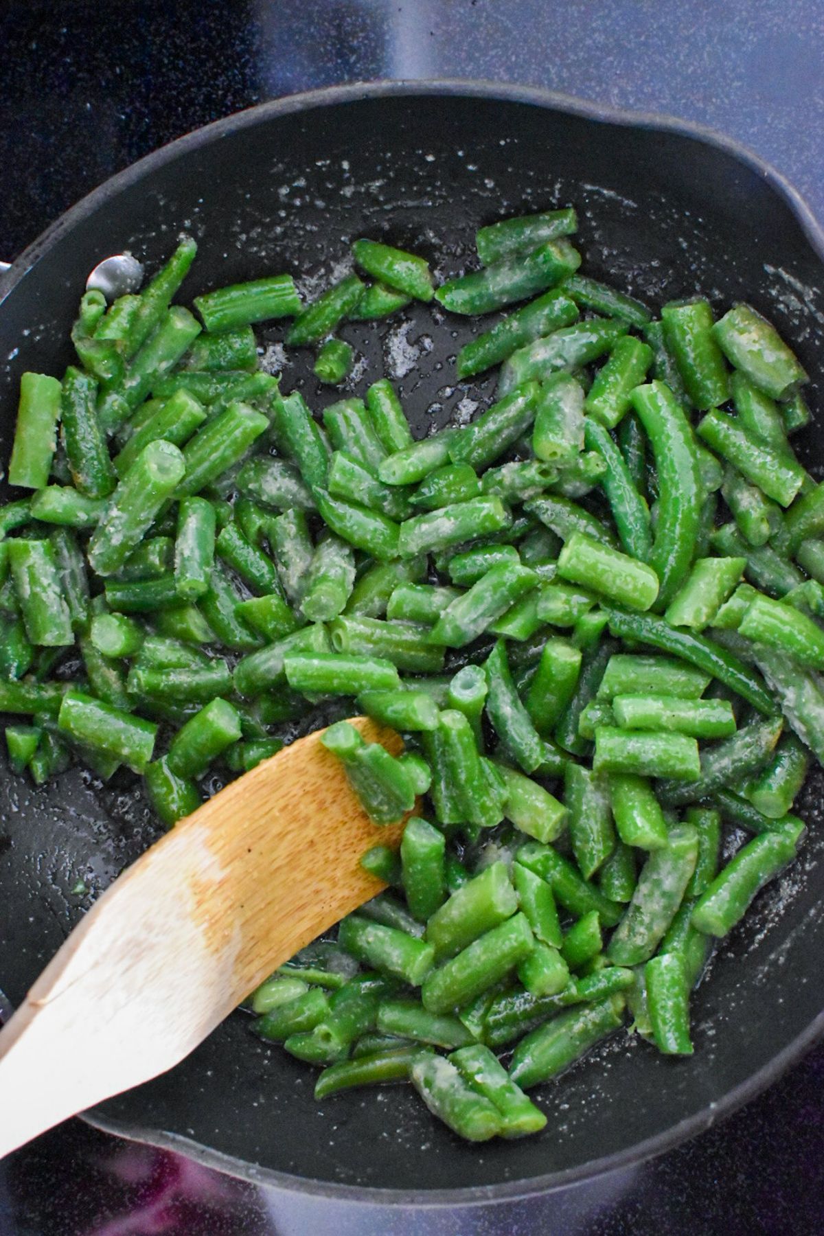 Green beans being mixed in a sauté pan with a wooden spoon.