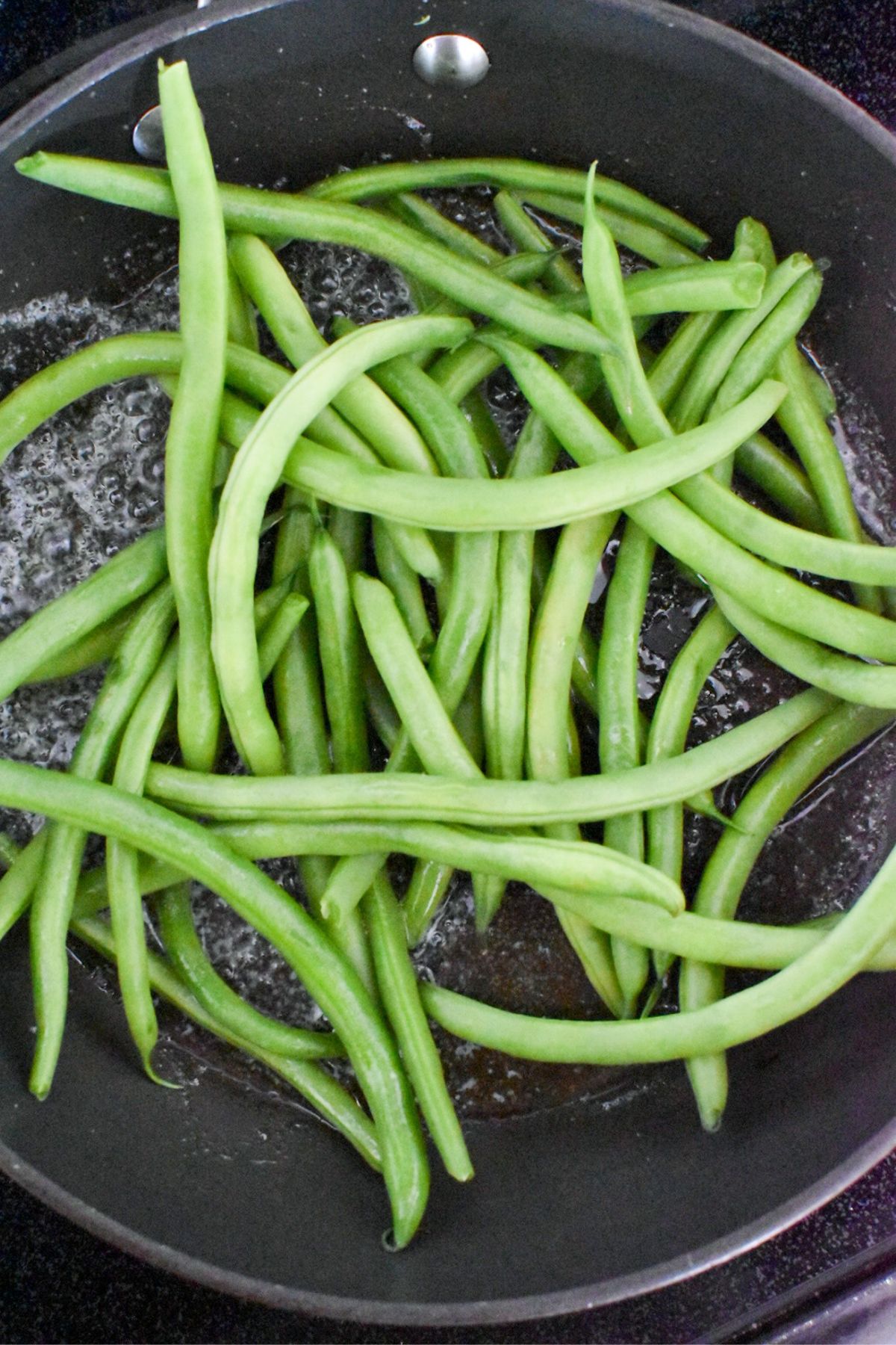 Fresh green beans in a sauté pan with butter and olive oil.