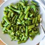 Cooked, seasoned green beans on a plate with fork on a wood table.