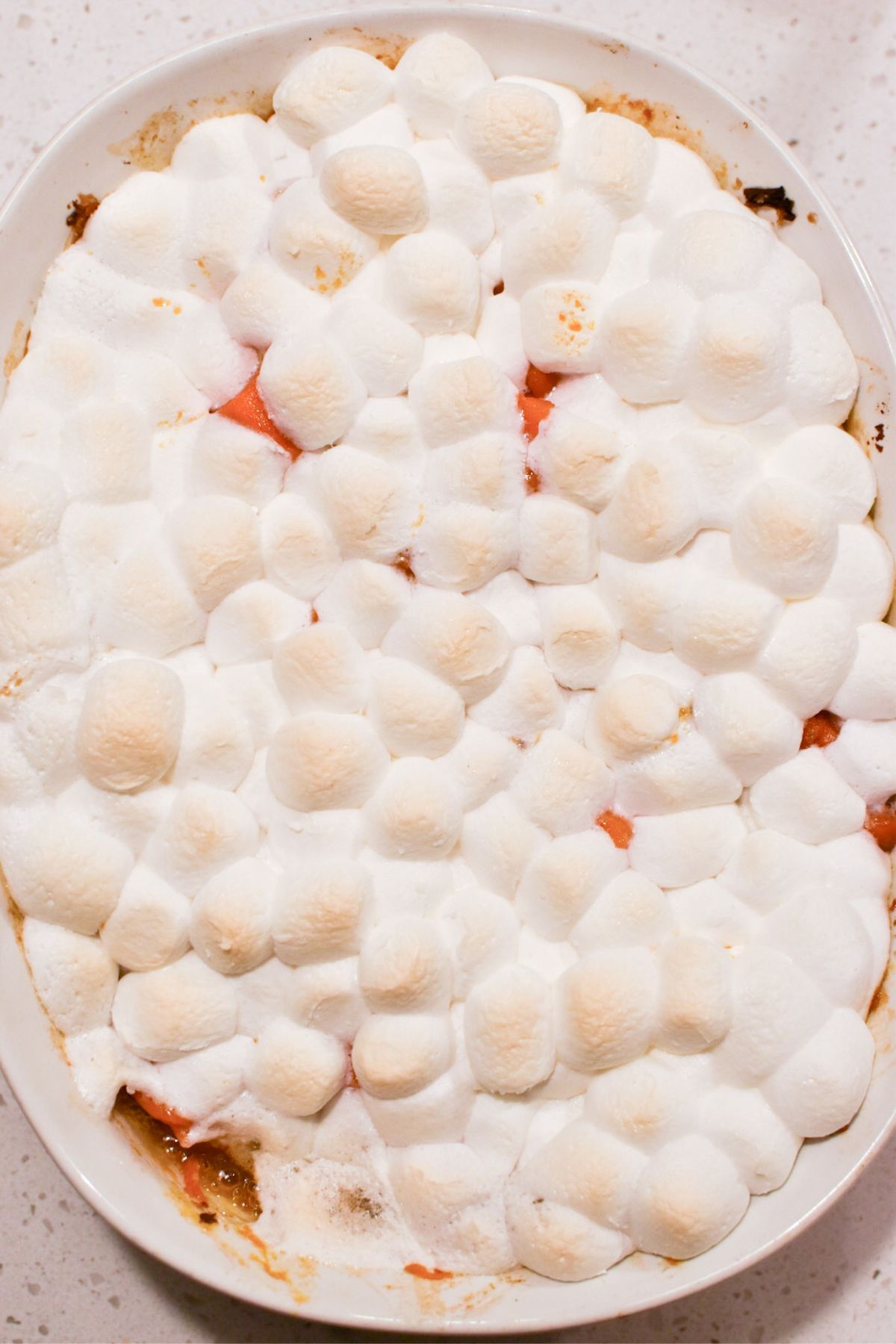 Candied yams with toasted marshmallows on top in a white casserole dish.