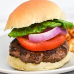A picture of a burger on a bun with tomato, red onion and lettuce.