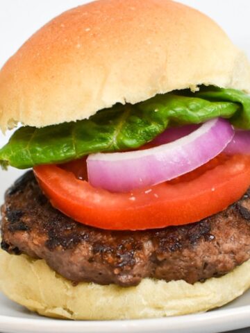 A picture of a burger on a bun with tomato, red onion and lettuce.