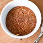 Chili seasoning in a small white bowl with a spoon next to it.