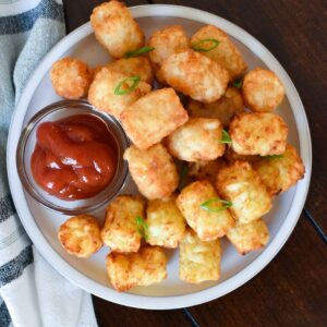 A plate of potato puffs with green onions on top and ketchup in a small dish.