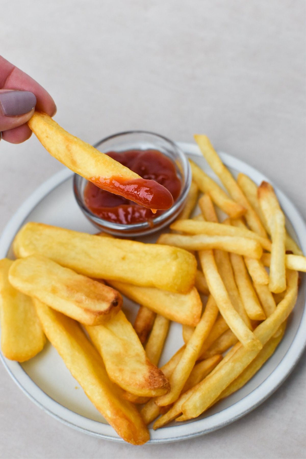 A french fry dipped in ketchup above a plate of steak fries and shoestring french fries.