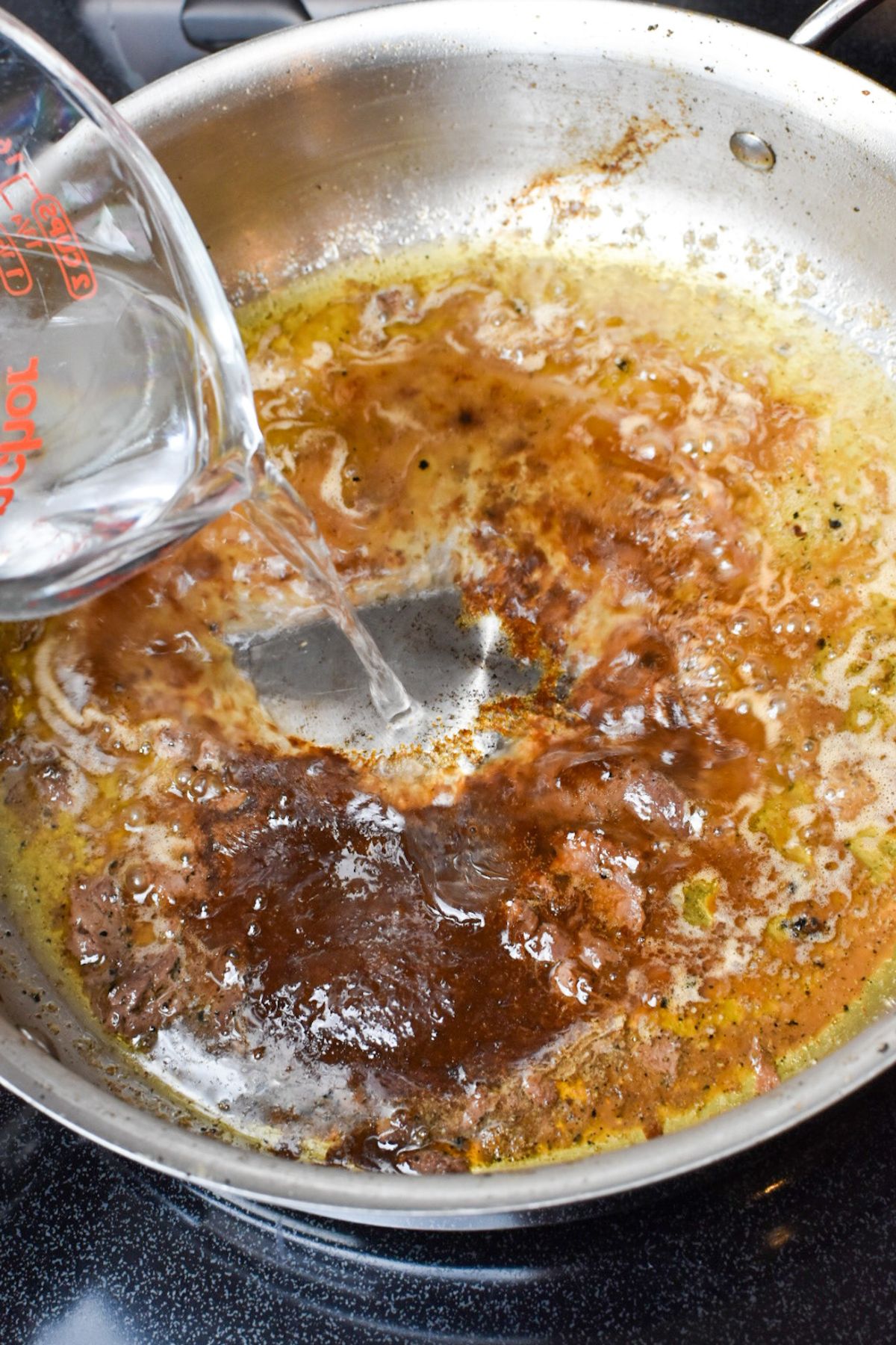 Adding water and beef bouillon to the beef drippings to make gravy.