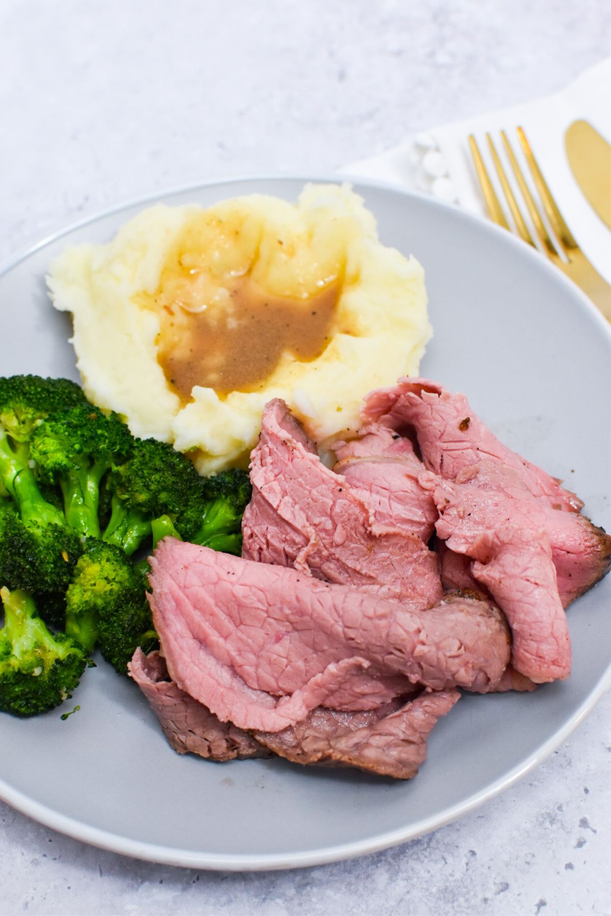 A plate with roast beef, sautéed broccoli, mashed potatoes and gravy on it.