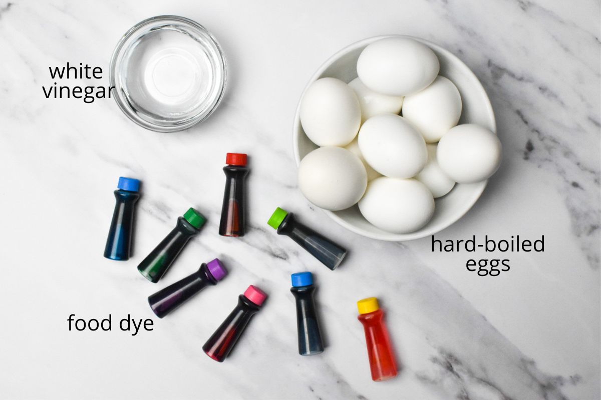 Hardboiled eggs, food dye, and white vinegar on a marble counter.
