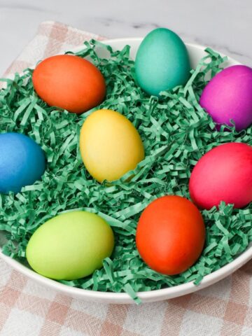 The colored eggs on green Easter grass in a white bowl.