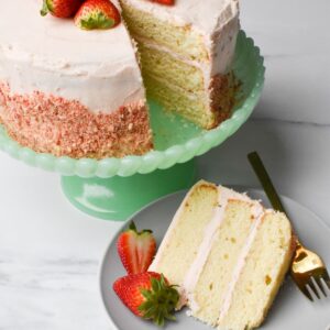 Strawberry crunch cake with a slice on a plate with a couple of strawberries next to it.