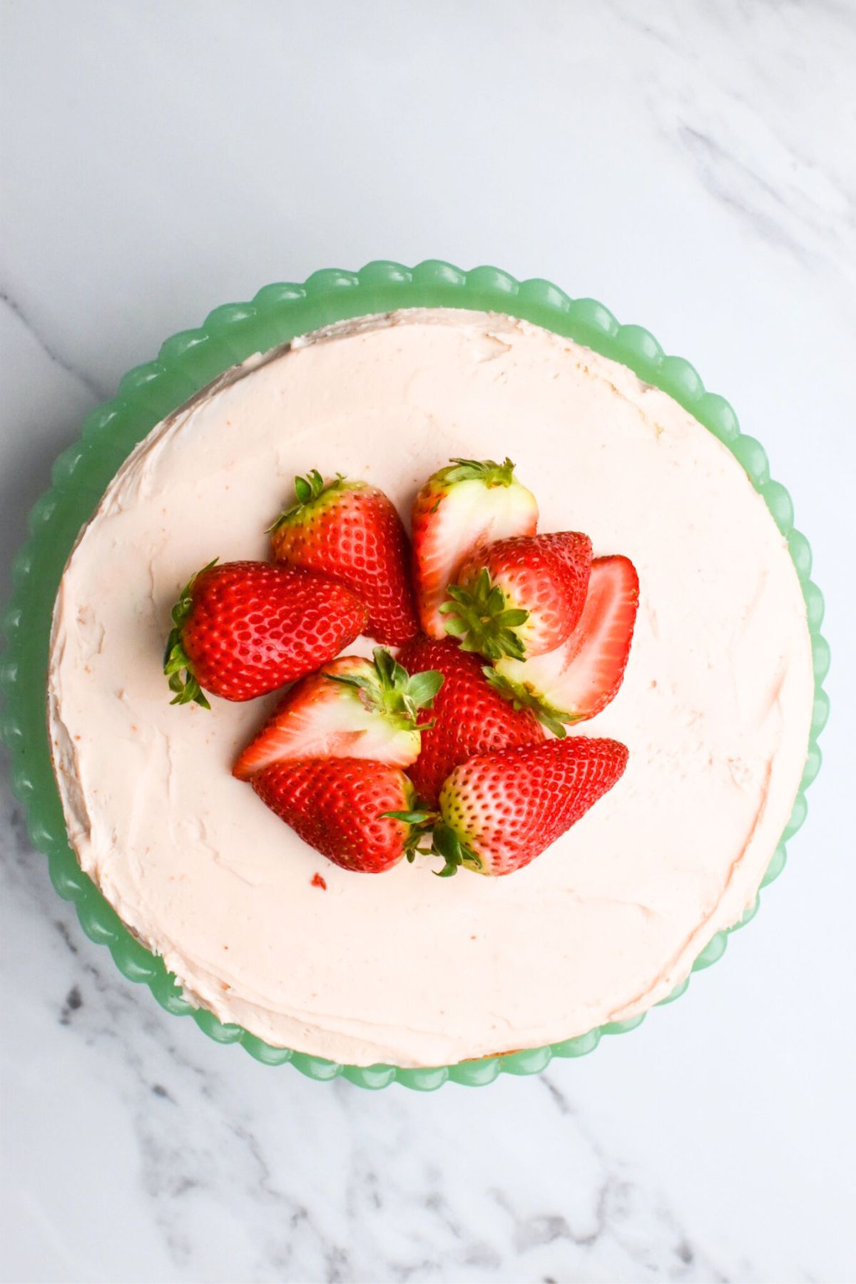 Top view of a strawberry crunch cake with light pink strawberry frosting and sliced strawberries on top.