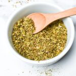 Homemade Italian seasoning mix in a small white bowl and wooden spoon