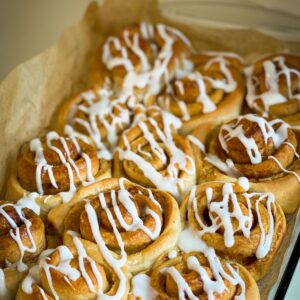 Cinnamon rolls in a pan with parchment paper with white icing drizzled on them.