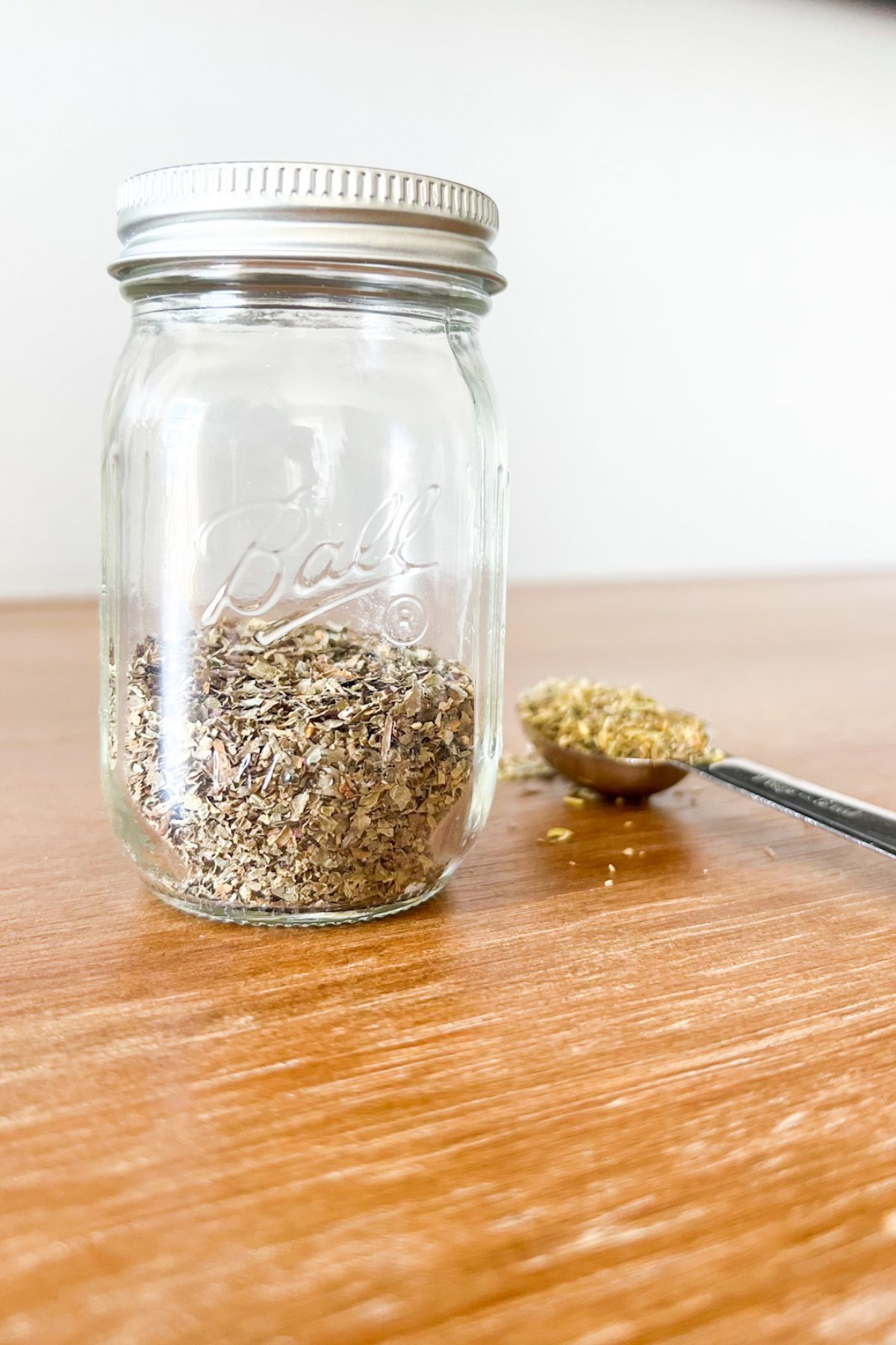 Italian seasoning in a small class jar and a measuring spoon in the background.