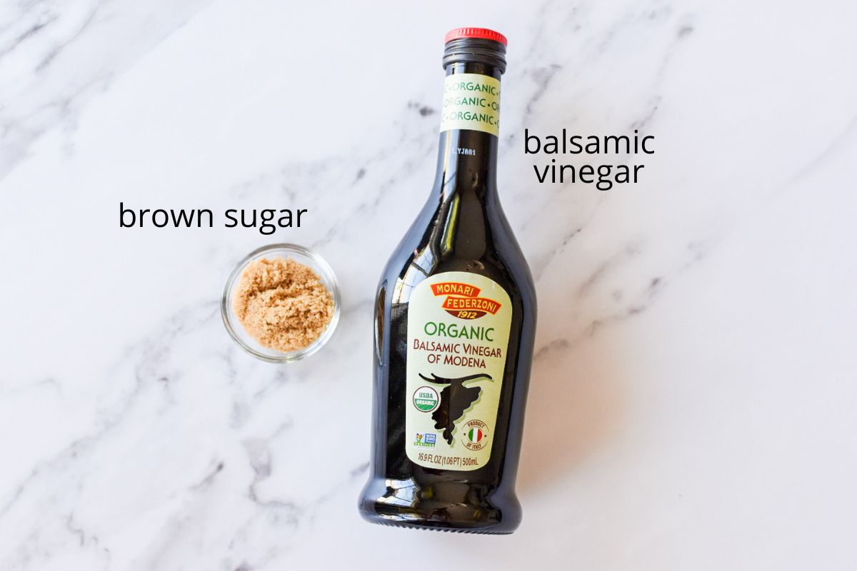 A bottle of balsamic vinegar and a small glass bowl of brown sugar.