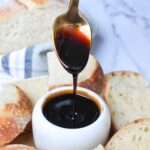 Caramelized balsamic vinegar being drizzled into a small white bowl with bread in the background.