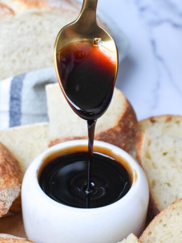 Caramelized balsamic vinegar being drizzled into a small white bowl with bread in the background.