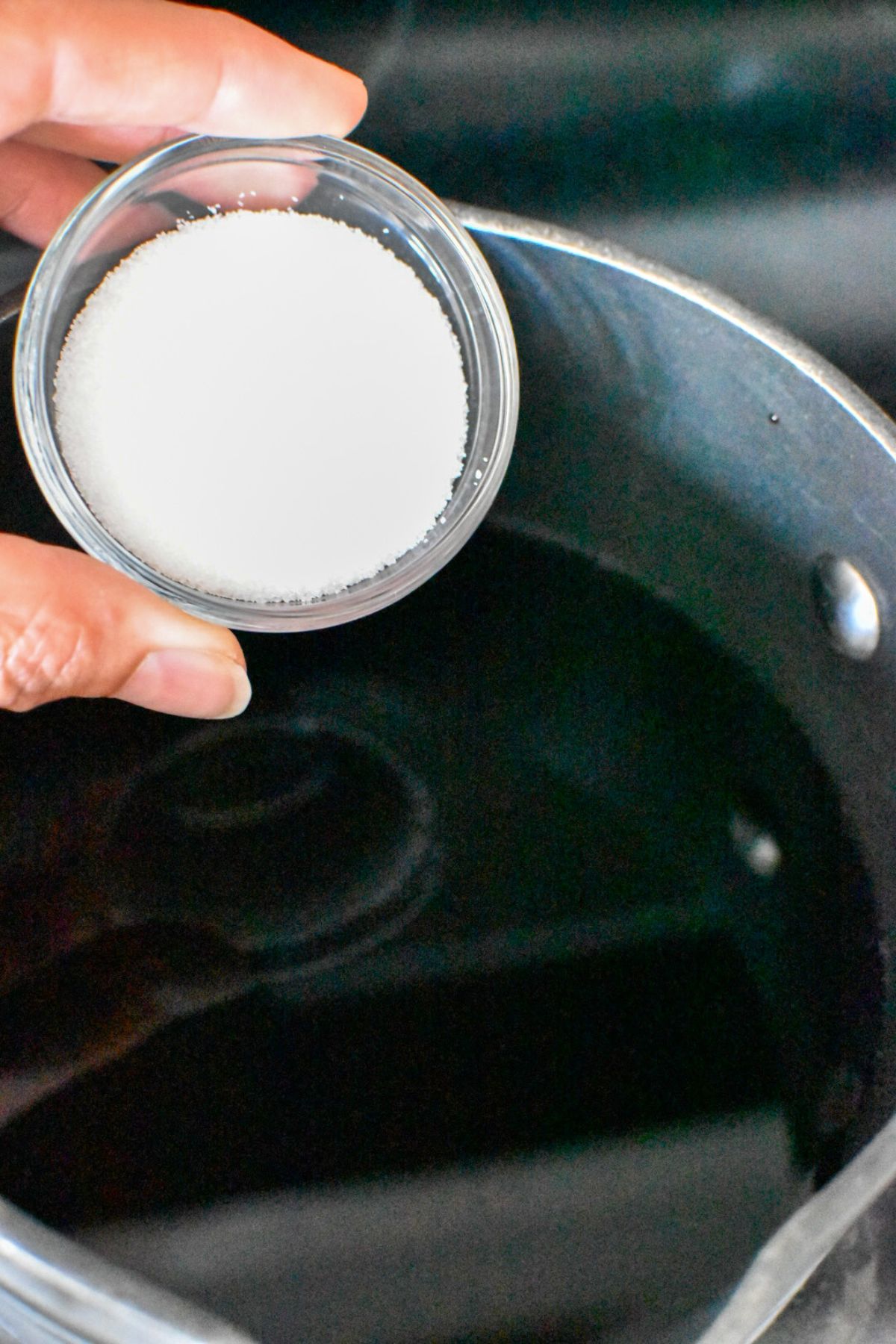 A small bowl of white sugar being added to a small saucepan of balsamic vinegar.